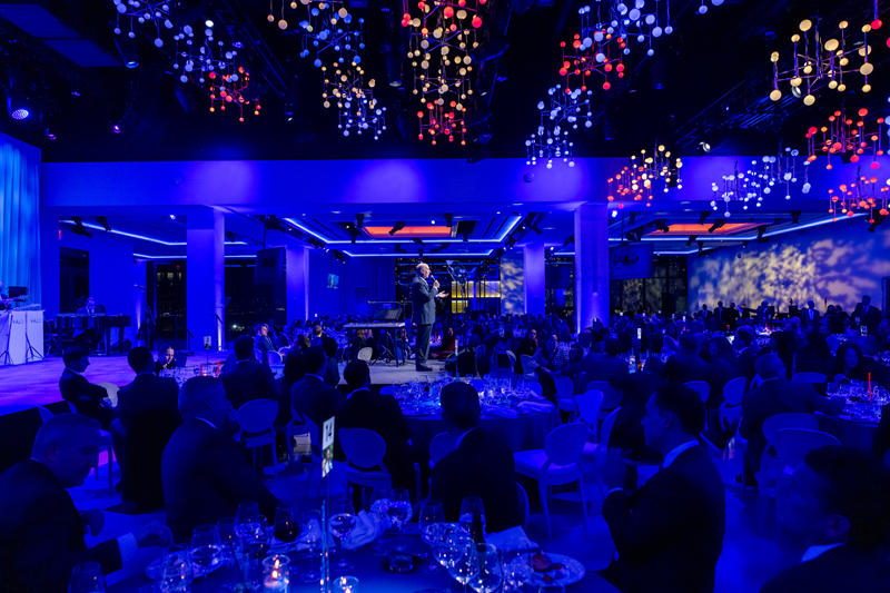 ambient lighting in a room with gala attendees facing the main stage and looking at speaker
